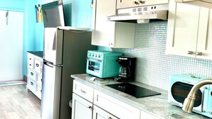 A kitchen with white cabinets, a stainless steel refrigerator, a teal oven, and a coffee maker.