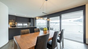 Un espace repas moderne avec une table et des chaises en bois, une cuisine en arrière-plan et une grande fenêtre donnant sur un pont.