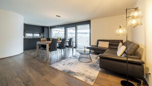 Un salon moderne avec un canapé, une table à manger et des chaises. Il y a un balcon avec vue sur la ville.