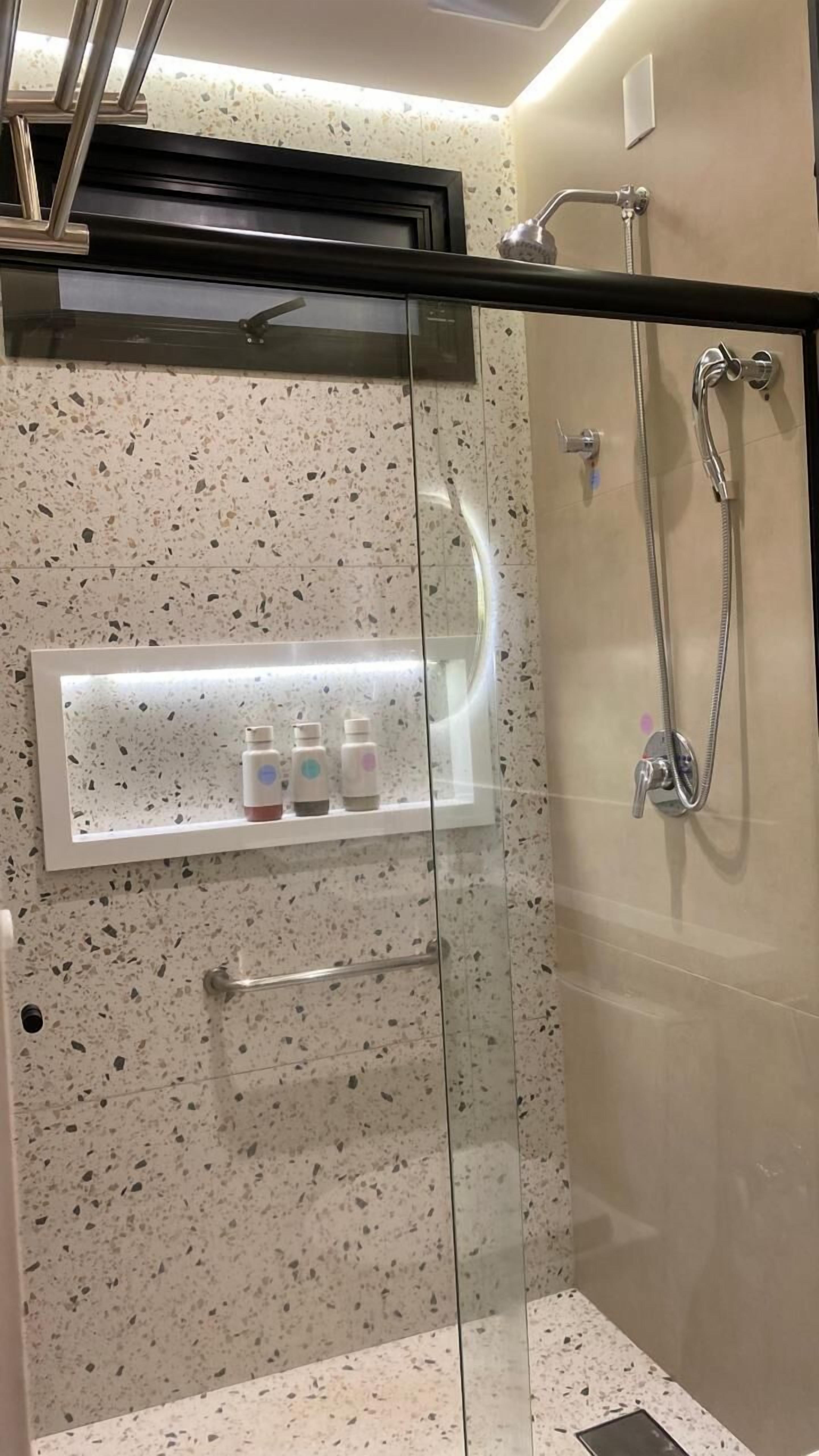 A glass-enclosed shower with a handheld showerhead and a wall-mounted faucet.