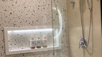 A glass-enclosed shower with a handheld showerhead and a wall-mounted faucet.