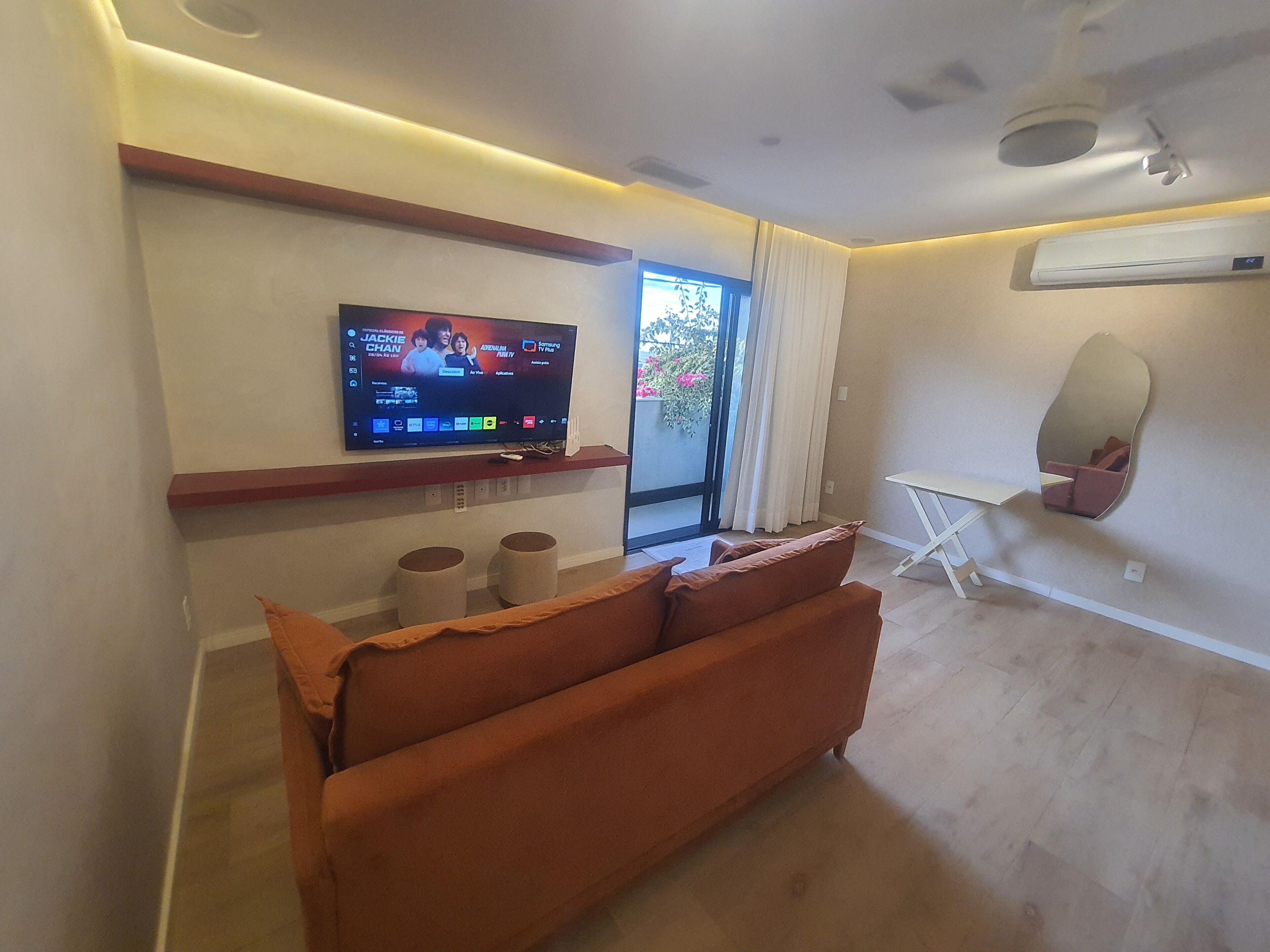 Uma sala de estar moderna com televisão de tela plana, sofá, mesa pequena e espelho grande.