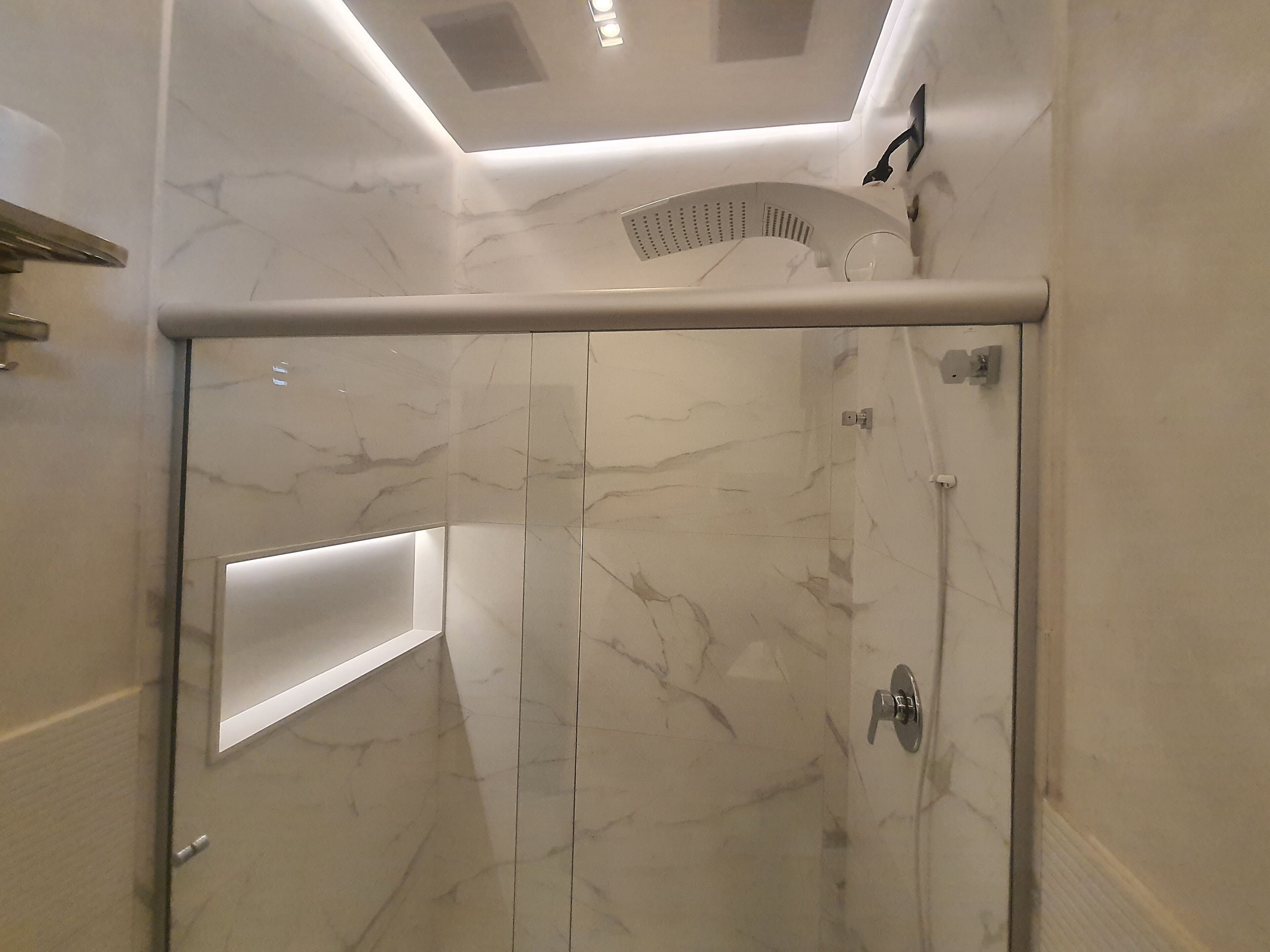 Um chuveiro moderno com porta de vidro, paredes de mármore e luminária no teto.