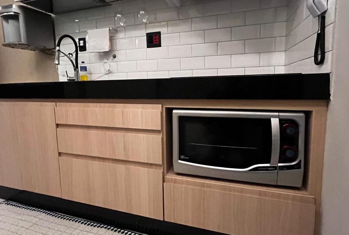 Una cocina con horno empotrado, armarios de madera, encimera negra y salpicadero de azulejos blancos.
