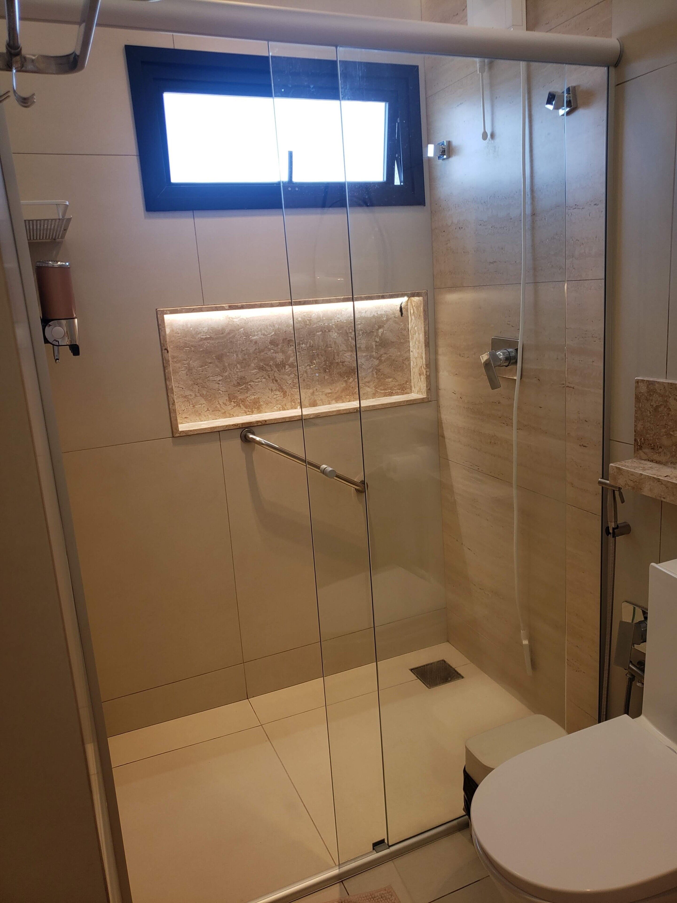 A modern bathroom with a glass shower enclosure, a small window, and a toilet.