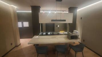 Uma cozinha moderna com uma ilha central, forno embutido e uma pia. Há três cadeiras ao redor da ilha.