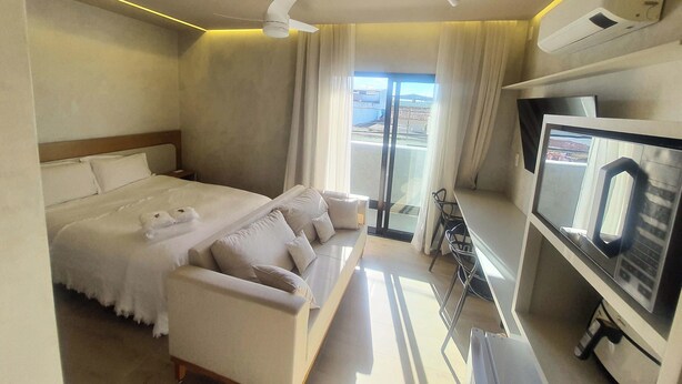 A hotel room with a bed, a sofa, a TV, and a window with curtains. - Apart-hotel Theotókos Flats (Piumhi)