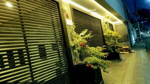 A building with closed shutters, potted plants with red flowers, and a paved sidewalk. - Apart-hotel Theotókos Flats (Piumhi)