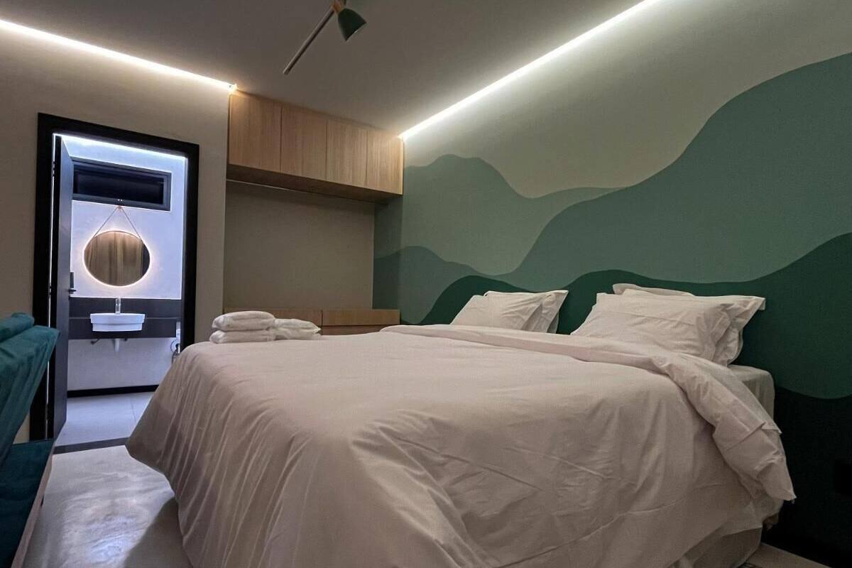 Une chambre moderne avec un grand lit, une table de chevet, un miroir et une vue sur l’extérieur.