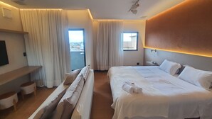 A modern hotel room with a large bed, a sofa, a small table, and a window with a view. - Apart-hotel Theotókos Flats (Piumhi)