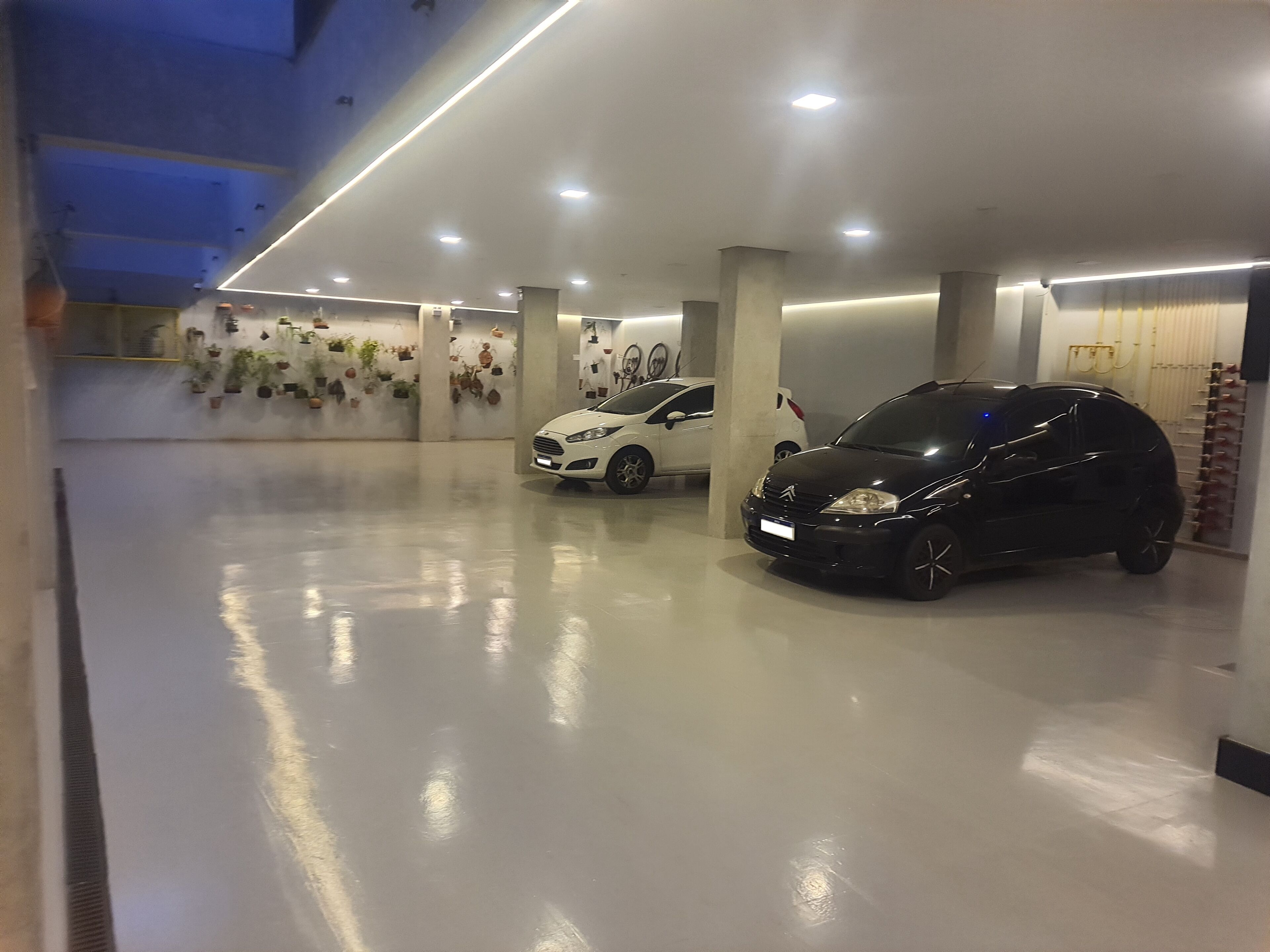 A parking garage with two cars parked, concrete pillars, and a ceiling with recessed lighting.