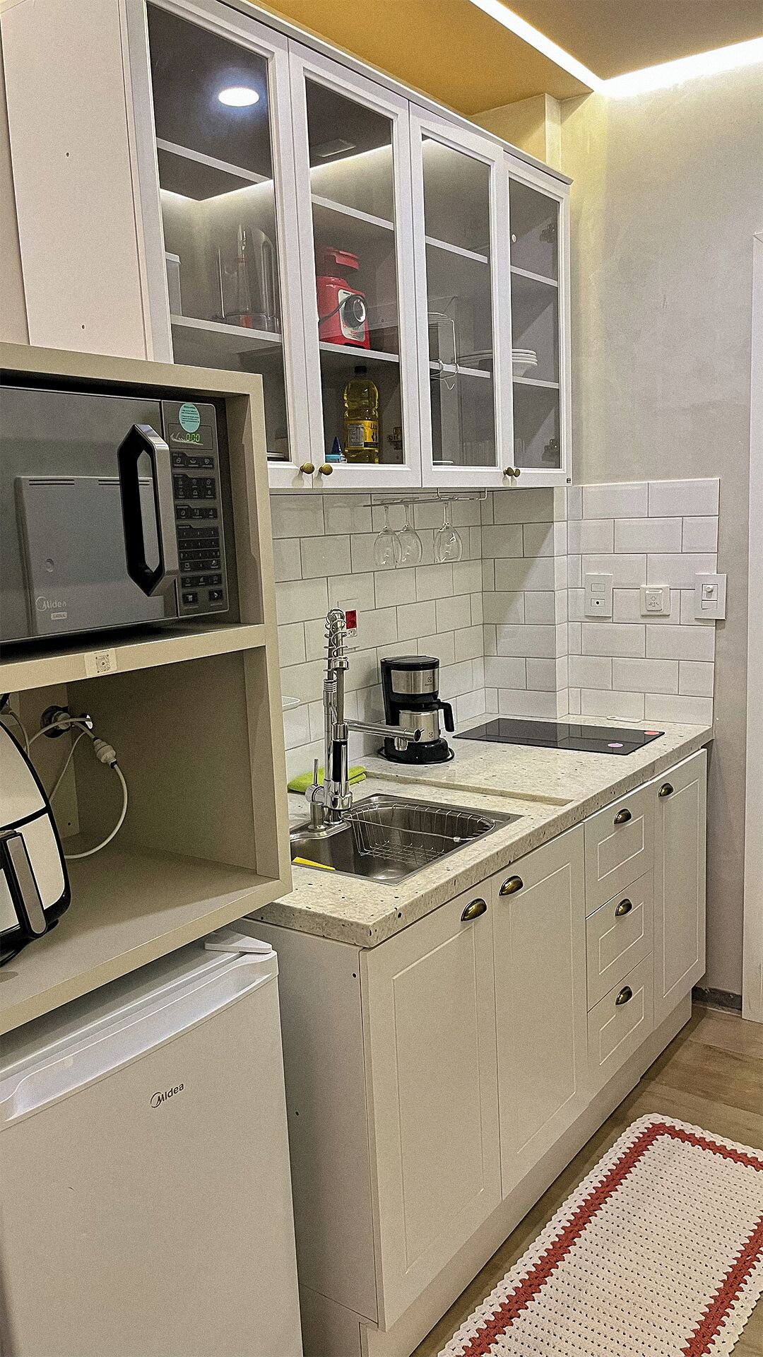 Una cocina con armarios blancos, un microondas, una cafetera y un lavabo.