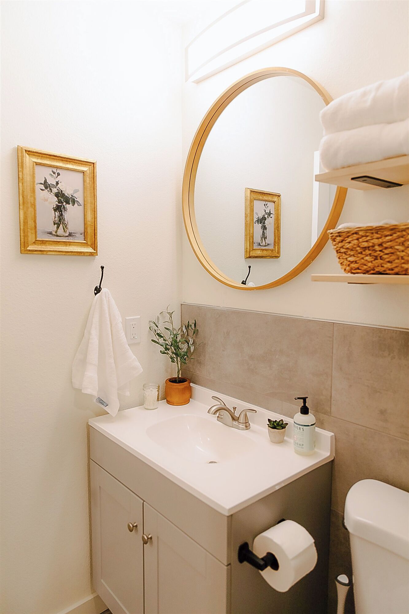 Un baño con un lavamanos blanco, un espejo, toallero, planta en maceta y un inodoro.