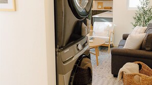 Ein kompakter Waschbereich mit einer Frontlader-Waschmaschine und -Trockner, ein Essbereich mit Tisch und Stühlen sowie eine gemütliche Sitzecke mit einer Couch und Kissen.