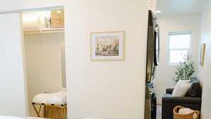 Ein Schlafzimmer mit Bett, Nachttisch mit Blumenvase, Teppich und einem Flur, der in einen Wohnbereich mit Sofa und Pflanze führt.