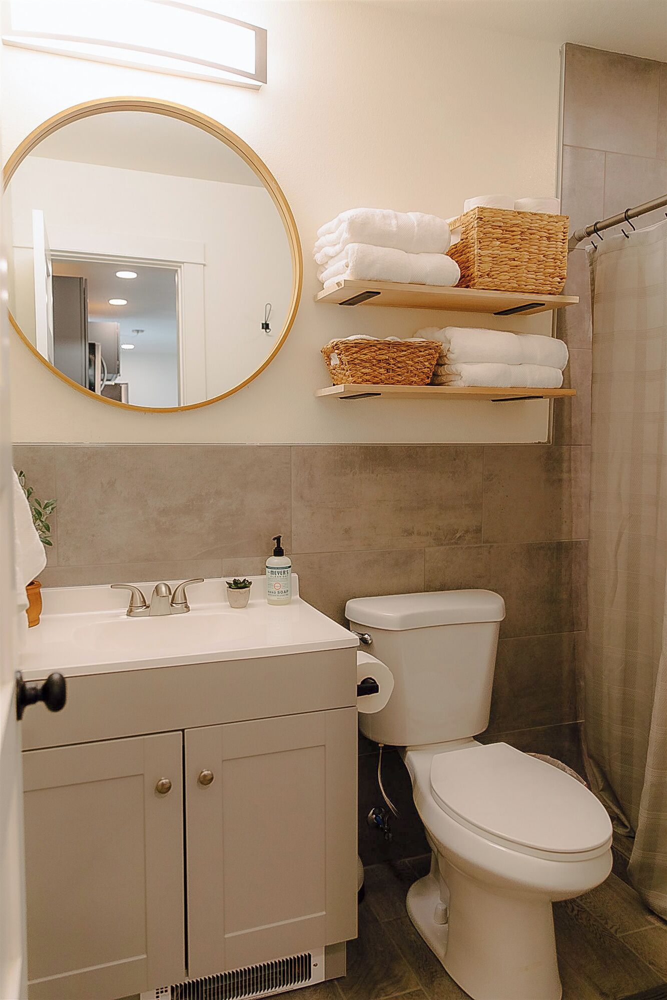 A bathroom with a toilet, sink, mirror, and towel storage.