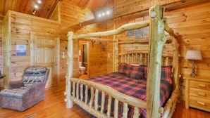 A log cabin bedroom with a four-poster bed, a chair, and a wooden nightstand. - Pet-Friendly Townsend Mtn Cabin w/ Hot Tub & Daybed Patio (Townsend)