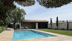 A swimming pool with a stone deck, a stone building with a tiled roof, and a stone wall.