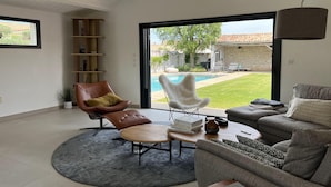 A modern living room with a pool view, a leather chair, a sofa, and a wooden coffee table.
