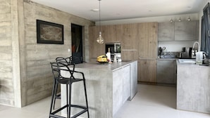 A modern kitchen with a central island, bar stools, and a hanging light fixture.