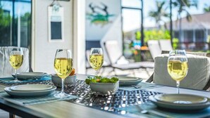 A dining table set with white wine glasses, plates, and a bowl of greens, with a view of a house and palm trees in the background. - Flamingo House - with  Boat dock & Kayak & Fenced (Cape Coral)