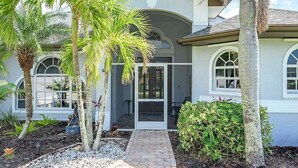 A two-story house with a covered patio, palm trees, and a small garden. - Flamingo House - with  Boat dock & Kayak & Fenced (Cape Coral)