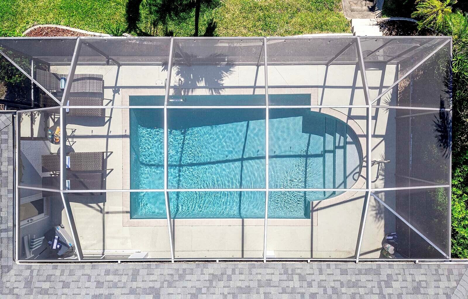 Une piscine entourée d’une paroi en verre, bordée d’une terrasse en briques et agrémentée de mobilier d’extérieur.