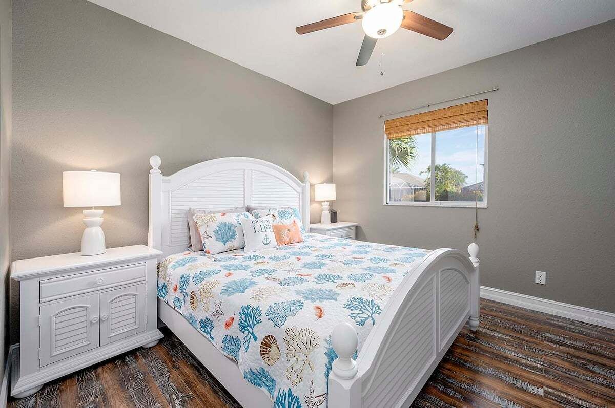 A bedroom with a bed, nightstands, a ceiling fan, a window with a view, and a wooden floor.