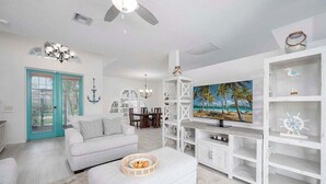 A living room with a white sofa, a television, and a painting of a beach scene. - Flamingo House - with  Boat dock & Kayak & Fenced (Cape Coral)