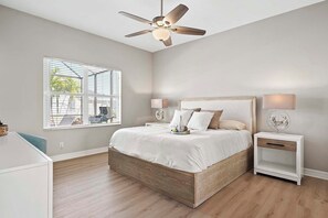 Ein Schlafzimmer mit einem Bett, Nachttischen, einem Deckenventilator und einem Fenster mit Jalousien.