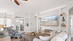 Un salon spacieux doté d’une grande télévision, de sièges confortables et offrant une vue sur la plage par la fenêtre.