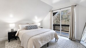 Ein Schlafzimmer mit einem großen Bett, einem Nachttisch, einem Fenster mit Vorhängen und Blick ins Freie.