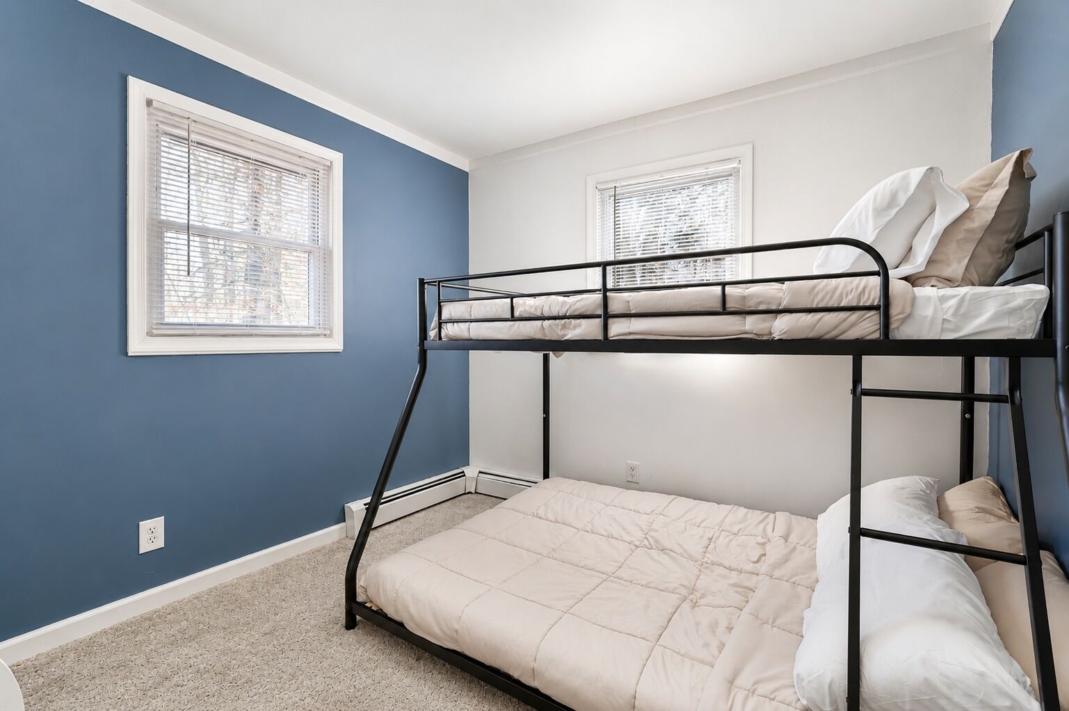 Een slaapkamer met stapelbed, een blauwe muur, witte plinten en een vloerbedekking.