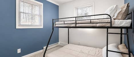 Een slaapkamer met stapelbed, een blauwe muur, witte plinten en een vloerbedekking.
