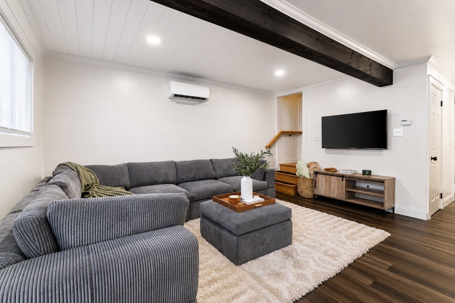 A modern living room with a sectional sofa, a coffee table, a flat-screen TV, and a staircase leading to another level.