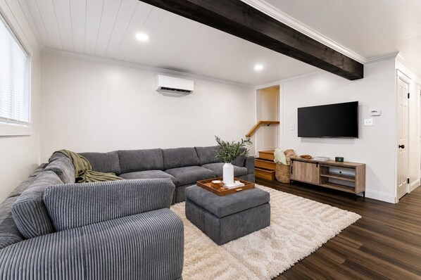 A modern living room with a sectional sofa, a coffee table, a flat-screen TV, and a staircase leading to another level.