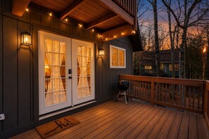 Une terrasse en bois avec un barbecue, une véranda couverte dotée de portes vitrées et des guirlandes lumineuses.