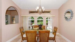 A dining area with a glass table surrounded by wicker chairs, a chandelier, and a large mirror on the wall. - Alecia -Gulf access Home (Cape Coral)