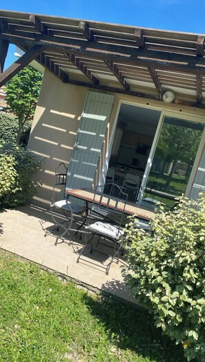 A covered patio area with a table and chairs, a sliding glass door, and a view of the surrounding greenery.