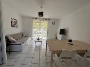 A room with a sofa, a dining table with chairs, a television, and a clock on the wall.