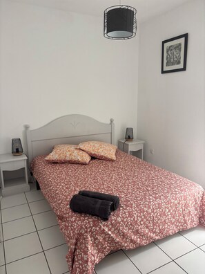 A bed with floral bedding, two pillows, a black towel, and a hanging light fixture.