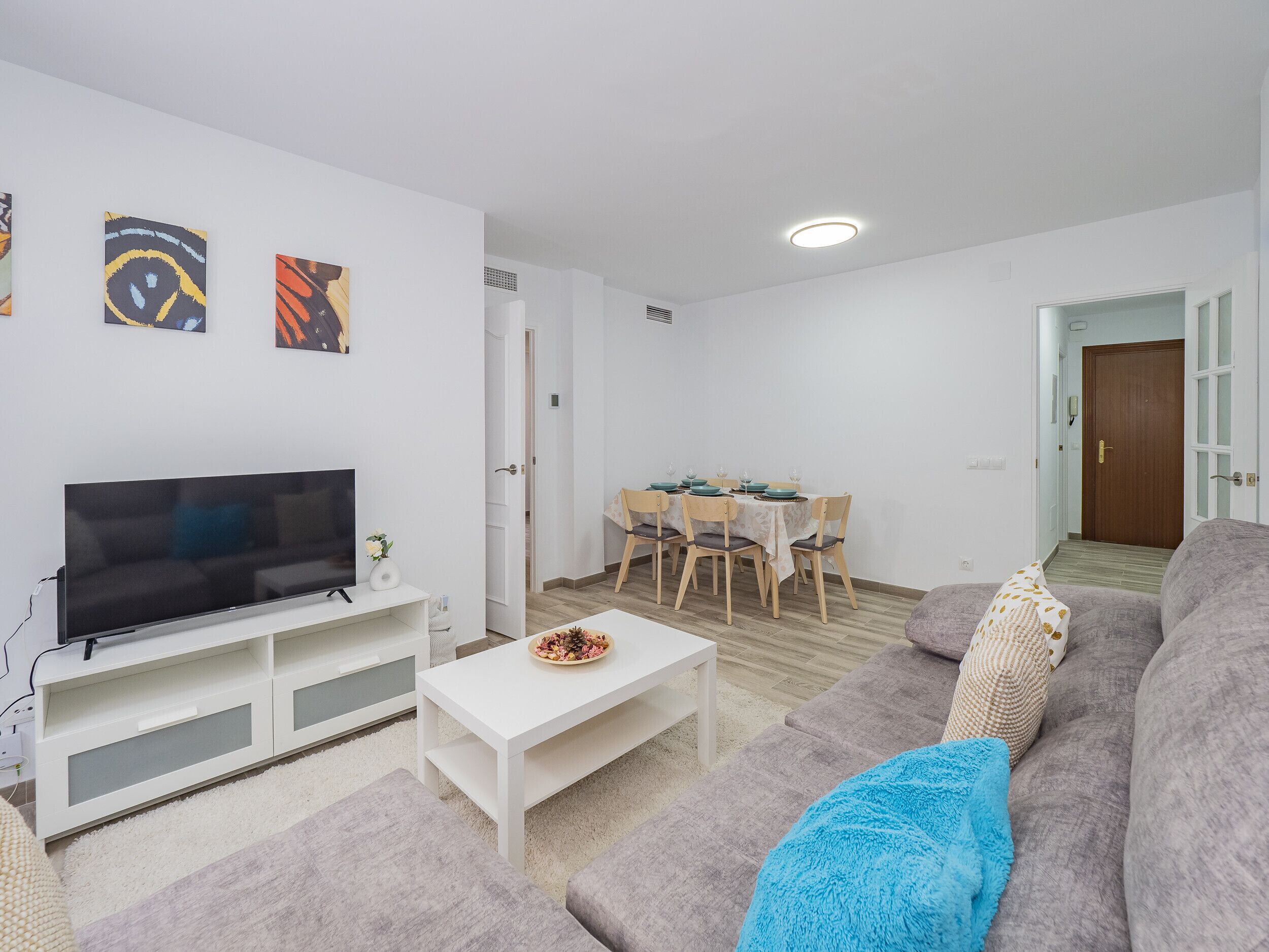 Ein modernes Wohnzimmer mit einem Flachbildfernseher, einem Esstisch mit Stühlen, einem grauen Sofa und einem weißen Couchtisch.