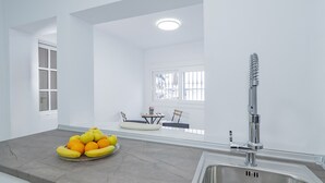 A modern kitchen with a stainless steel sink, a fruit bowl on the counter, and a dining area in the background.