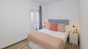 A bedroom with a bed, bedside tables, a nightstand, a window with curtains, and a view of the outside.