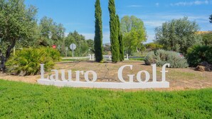 A sign for "Lauro Golf" with a clear view of the surrounding landscape, including trees and a pathway.