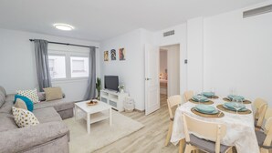 A modern living room with a sofa, TV, and dining area with chairs and a table set for four.