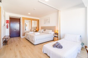 A hotel room with two beds, a desk, and a chair. There is a fire extinguisher and an exit sign on the wall.