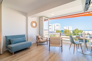 Un salón moderno con un sofá azul, un sillón color beige y una mesa de comedor para dos personas.