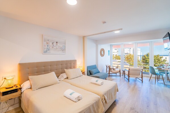 A hotel room with two beds, a dining area with chairs, a table, and a balcony with a view.