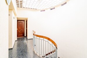 Un pasillo con una puerta de madera al final, una barandilla curva y un suelo de baldosas.
